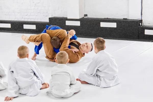 Teacher, professional judo, jiu jitsu coach training kinds, boys, showing exercises. Children learning indoors. Attentive kids. Concept of martial arts, combat sport, sport education, childhood