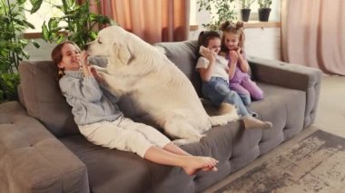 Happy smiling girl, kid playing with cute golden retriever dog on sofa. Children talking on phone. Comfort. Concept of family, childhood, pets, care, friendship, emotions. leisure