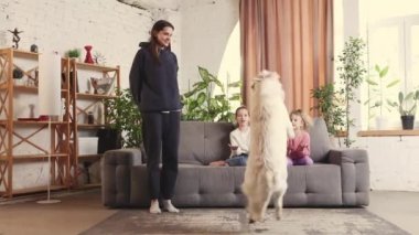 Smart, trained golden retriever dog playing with kids and young woman in living room. Catching toy in a jump. Concept of family, childhood, pets, care, friendship, emotions. leisure