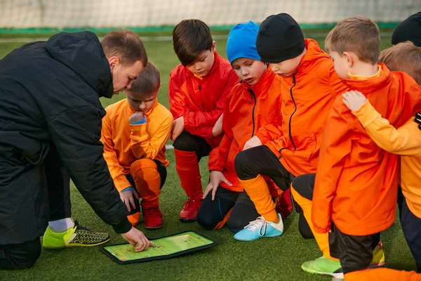 Education. Group of boys, children training football with professional coach on field outdoors. Man showing sportive tactics. Concept of sport, childhood, active lifestyle, hobby, sport club