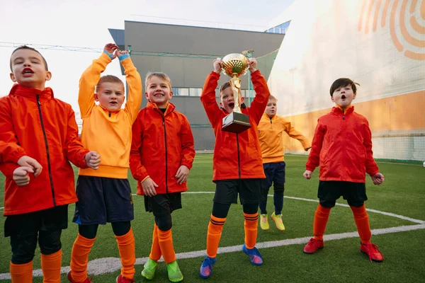 Happy champions. Group of little boys, children in uniform, football players raising award, trophy. Kids training on outdoor playground. Sport, childhood, active lifestyle, hobby, sport club concept