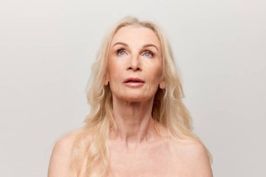 Portrait of beautiful middle-aged, mature woman with well-kept natural skin posing over grey studio background. Concept of natural beauty, face skin care, cosmetology and cosmetics, health