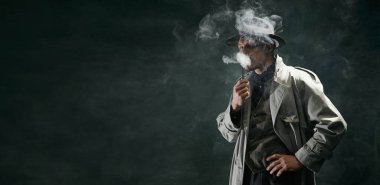 Portrait of man, detective in trench coat and hat smoking pipe over vintage dark green background. Banner. Concept of occupation, character, history. Retro style. Copy space for ad
