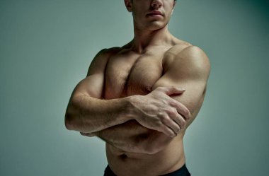 Cropped image of strong muscular male body, shoulders, hands and breast over pale green studio background. Male model posing shirtless. Concept of mans beauty, sportive and healthy lifestyle, fashion