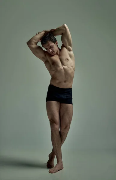 Full-length portrait young man with strong relief muscular body posing shirtless in black underwear over studio background. Statue pose. Concept of mans beauty, sportive and healthy lifestyle