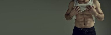 Cropped image of muscular relief body, torso. Male model posing in singlet over green studio background. Banner. Concept of mans beauty, sportive and healthy lifestyle, fashion. Copy space for ad