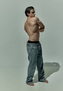 Full-length image of handsome young man with strong muscular body shape posing over grey studio background. Concept of mans beauty, sportive and healthy lifestyle, fashion