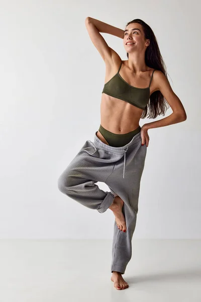 Happiness. Beautiful smiling young girl with slim, fit body posing in underwear and oversized pants over grey studio background. Natural beauty, weight loss, body-positivity, wellness, body care