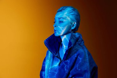 Lightning. Portrait of young blonde girl with abstract neon stripes on body posing over orange background in blue neon lights. Concept of art, modern style, cyberpunk, futurism and creativity