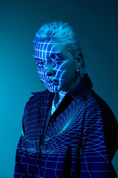 Virtual reality. Portrait of young blonde girl with neon stripes on face posing over dark background in blue neon lights. Concept of art, modern style, cyberpunk, futurism and creativity