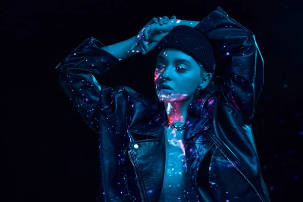 Portrait of young blonde girl with neon space holographic projection on body posing over dark background in blue neon lights. Concept of art, modern style, cyberpunk, futurism and creativity