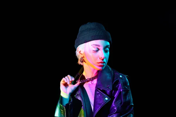 Portrait of young blonde girl with neon holographic colors on body posing over dark background in blue neon lights. Concept of art, modern style, cyberpunk, futurism and creativity