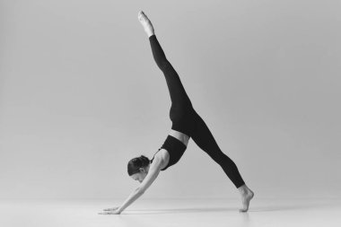 Standing on twine. Black and white photography. Young slim girl doing stretching exercises over studio background. Concept of sport, body care, beauty, fitness, active lifestyle. Ad