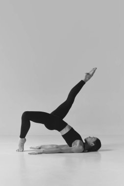 Balance and strength. Black and white photography. Young girl with strong slim body doing stretching, training on studio background. Concept of sport, body care, beauty, fitness, active lifestyle. Ad
