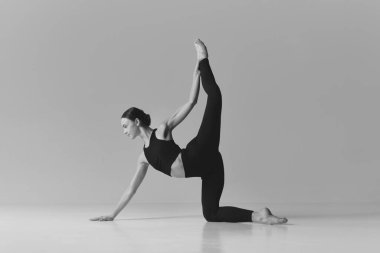 Strength. Black and white photography. Young flexible girl doing stretching exercises, training over studio background. Concept of sport, body care, beauty, fitness, active lifestyle. Ad