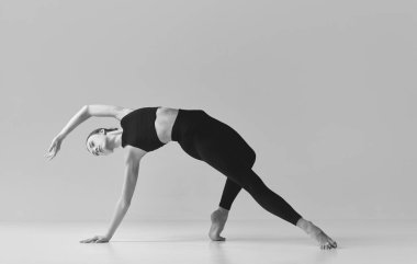 Flexibility. Black and white photography. Young slim, fit girl training, doing stretching exercises over studio background. Concept of sport, body care, beauty, fitness, active lifestyle. Ad