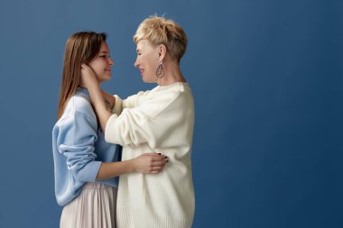 Portrait of happy beautiful middle-aged woman and her young daughter posing over blue studio background. Concept of motherhood, family, mothers day, love, emotions, relationship