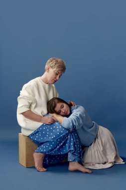Tender love. Portrait of beautiful middle-aged woman taking care after her young daughter, posing over blue studio background. Concept of motherhood, family, mothers day, love, emotions, relationship