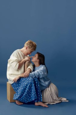 Cheerful and happy. Portrait of middle-aged woman and her young daughter posing over blue studio background. Concept of motherhood, family, mothers day, love, emotions, relationship