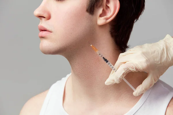 Chin fillers. Cropped image of young man doing cosmetological injections. Male model against grey studio background. Concept of mens health, skin care, hygiene and male cosmetological treatment