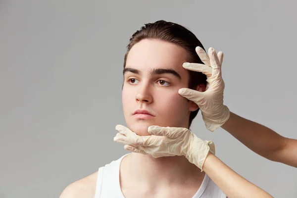 Face lifting. Portrait of young man taking care after skin with cosmetology. Male model against grey studio background. Concept of mens health, skin care, hygiene and male cosmetological treatment