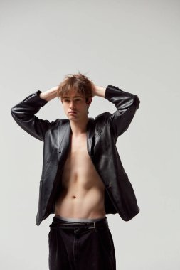 Male style. Handsome young man posing shirtless in leather jacket and black pants against grey studio background. Concept of mens health, modern fashion, beauty, style, body care