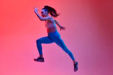 Full-length image of young girl, professional athlete, runner in motion, training over pink studio background in neon light. Concept of sportive lifestyle, health, endurance, action and motion. Ad