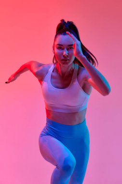 Front view dynamic portrait of young professional female runner, athlete training over pink studio background in neon light. Concept of sportive lifestyle, health, endurance, action and motion. Ad