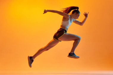 Speed. Dynamic image of young girl, professional athlete, runner in motion, training on orange studio background in neon light. Concept of sportive lifestyle, health, endurance, action and motion. Ad
