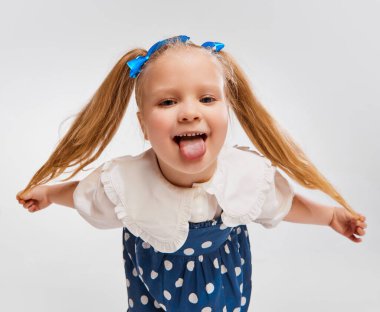 Positive playful mood. Beautiful cute little girl, child in retro style dress posing against grey studio background. Concept of childhood, game, emotions, activity, leisure time, retro style, fashion.