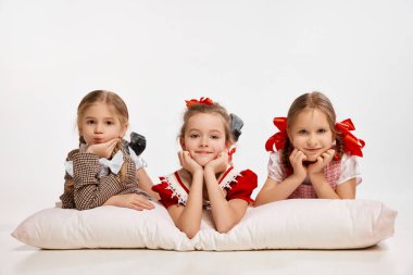 Relaxation and fun. Cute little beautiful girls, kids lying on big pillow against grey studio background. Concept of childhood, game, friendship, activity, leisure time, retro style, fashion.
