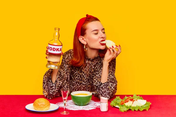 食品流行艺术摄影 美丽的红头发女人在黄色的背景下坐在桌旁吃饭 喝伏特加和洋葱沙拉 互补的颜色 文字的复制空间 — 图库照片