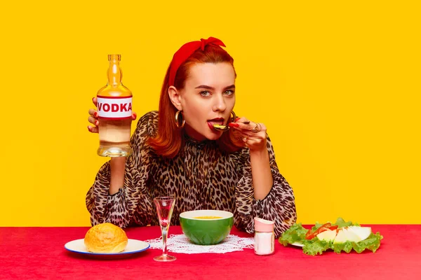 黄色の背景を背景にテーブルに座り チーズスープとウォッカを飲む美しいスタイリッシュな赤毛の女性 フードポップアート写真 補完的な色 広告のコピースペース — ストック写真