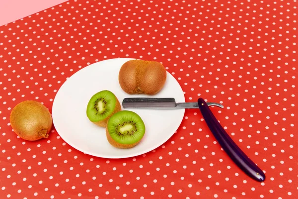 Plate with delicious kiwi and razor on red vintage tablecloth against pink studio background. Food pop art photography. Concept of creativity and art. Complementary colors. Copy space for ad, text