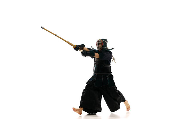 Мужчина, профессиональный кендо спортсмен в движении, в форме тренировки с бамбуковым мечом, синай на белом фоне студии. Концепция боевых искусств, спорта, японской культуры, действия и движения