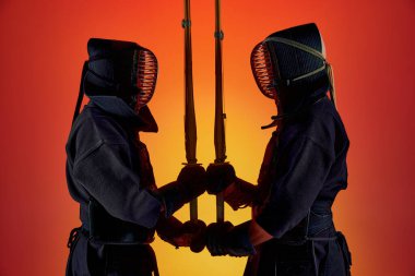 Kılıç kılıca. İki adam, profesyonel kendo dövüşçüsü, siyah üniformalı sporcular, neon ışıkta gradyan stüdyo geçmişine karşı antrenman yapıyorlar. Dövüş sanatları, spor, Japon kültürü, hareket kavramı