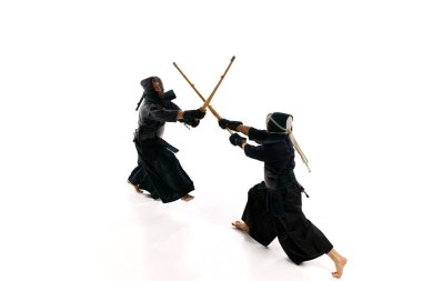 Üst Manzara. İki adamın dinamik görüntüsü, profesyonel kendo atletleri üniformalı ve beyaz stüdyo arka planına karşı shinai kılıcıyla antrenman yapıyorlar. Dövüş sanatları, spor, Japon kültürü, eylem, hareket