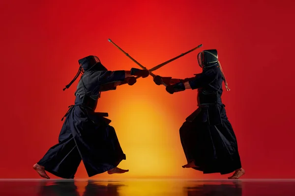 ネオンの光の中でグラデーションの赤いスタジオの背景に竹の新井剣でトレーニング2人の男性 プロの剣道選手のダイナミックなイメージ スポーツ 日本文化 運動の概念 — ストック写真