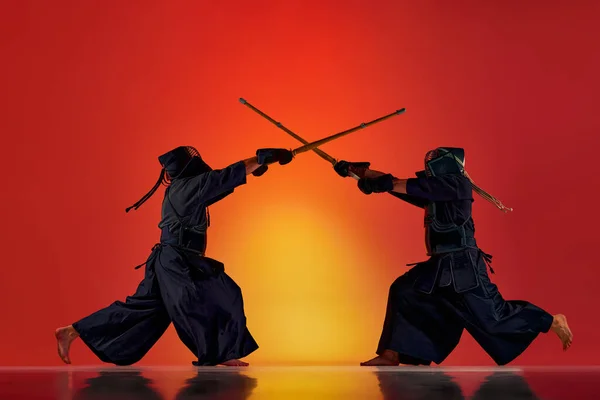 ネオンの光の中でグラデーションの赤いスタジオの背景に竹の新井剣でトレーニング2人の男性 プロの剣道選手のダイナミックなイメージ スポーツ 日本文化 運動の概念 — ストック写真