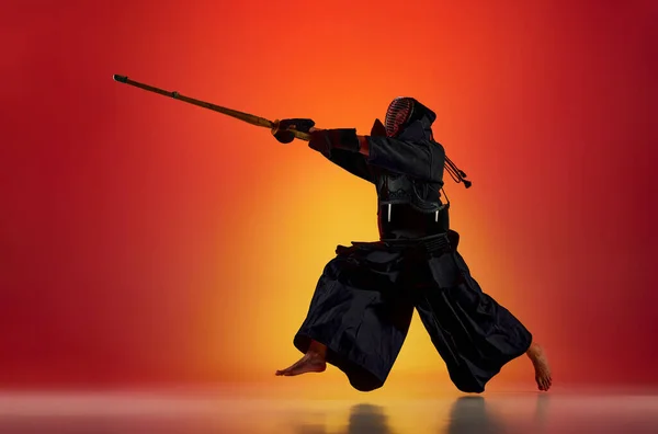 剣と黒のユニフォームを着たプロの剣道選手 ネオンの光の中でグラデーションの赤いスタジオの背景に対する新海の訓練 スポーツ 日本文化 アクション 動きの概念 — ストック写真
