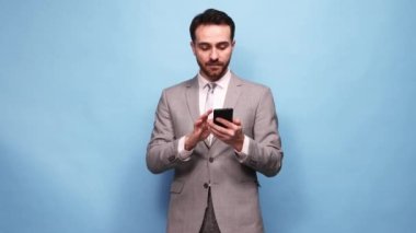 Resmi kıyafetli bir adam telefona bakıyor. Mavi stüdyo geçmişine karşı mutlu ve heyecanlı duygular besliyor. Haberler. İş, satış, bahis, duygu, dijital iletişim ve iş kavramı