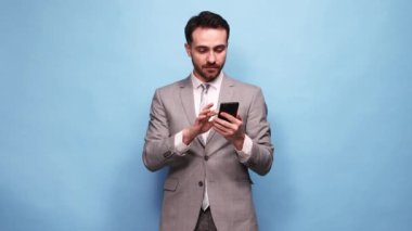 Duyguları kazanmak. Mutlu heyecanlı bir adam, takım elbiseli bir işadamı mavi stüdyo geçmişine karşı pozitiflikle telefon ekranına bakıyor. İş, satış, bahis, duygu, dijital iletişim ve çalışma