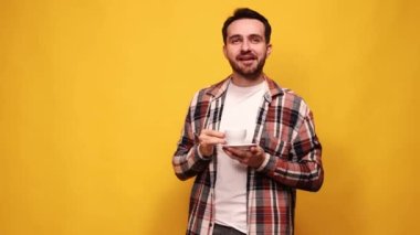 Kahve molası. Şık tişörtlü ve beyaz tişörtlü genç adam sarı stüdyo arka planında taze demlenmiş kahve içiyor. Pozitif enerji ve tat. Duyguların kavramı, yaşam tarzı, gelişigüzel
