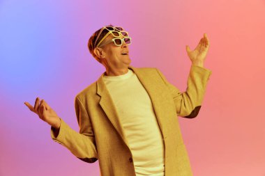 Tatil zamanı. Ceketli, olgun, orta yaşlı bir adamın portresi. Bir çok güneş gözlüğüyle neon ışıkta pembe arkaplanda poz veriyor. Duyguların kavramı, yaşam tarzı, yüz ifadesi, eğlence. Ad