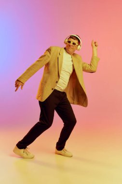 Ceketli olgun, orta yaşlı bir adamın portresi kulaklıkla müzik dinliyor, neon ışıkta pembe arkaplanda poz veriyor. Duyguların kavramı, yaşam tarzı, yüz ifadesi, eğlence. Ad