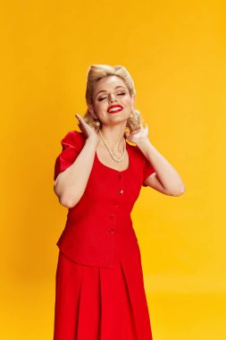 Pozitif kadınlık. Sarı stüdyo arka planında kırmızı elbiseli şık saçlı güzel bir genç kız. Eski moda anlayışı, güzellik, 50 'ler, 60' lar. Pin-up tarzı