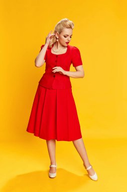 Kadınlık. Sarı stüdyo arka planında poz veren kırmızı takım elbiseli güzel sarışın kadın portresi. Eski moda anlayışı, güzellik, 50 'ler, 60' lar. Pin-up tarzı
