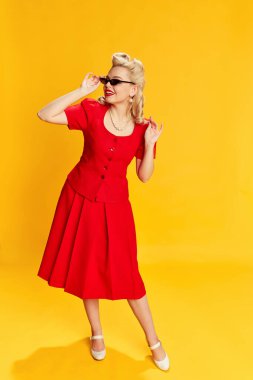 Kırmızı takım elbiseli, sarı stüdyo arka planında son moda güneş gözlüklü güzel sarışın kadın portresi. Eski moda anlayışı, güzellik, 50 'ler, 60' lar. Pin-up tarzı