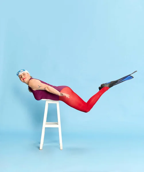 保持平衡 身穿游泳衣和红色紧身衣 头戴拖鞋在椅子上 背对着蓝色工作室背景的全长女性形象 面部表情 生活方式和时尚的概念 — 图库照片