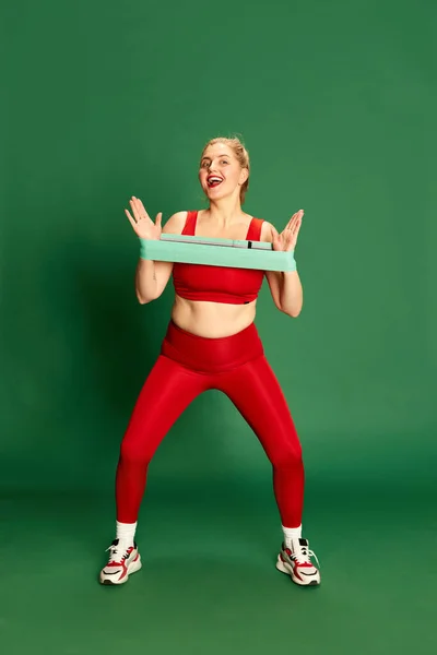 赤いスポーツ服を着た女性の完全な長さの肖像画 緑のスタジオの背景に対してフィットネス弾性バンドとトレーニング スポーツ 体重減少の概念 — ストック写真